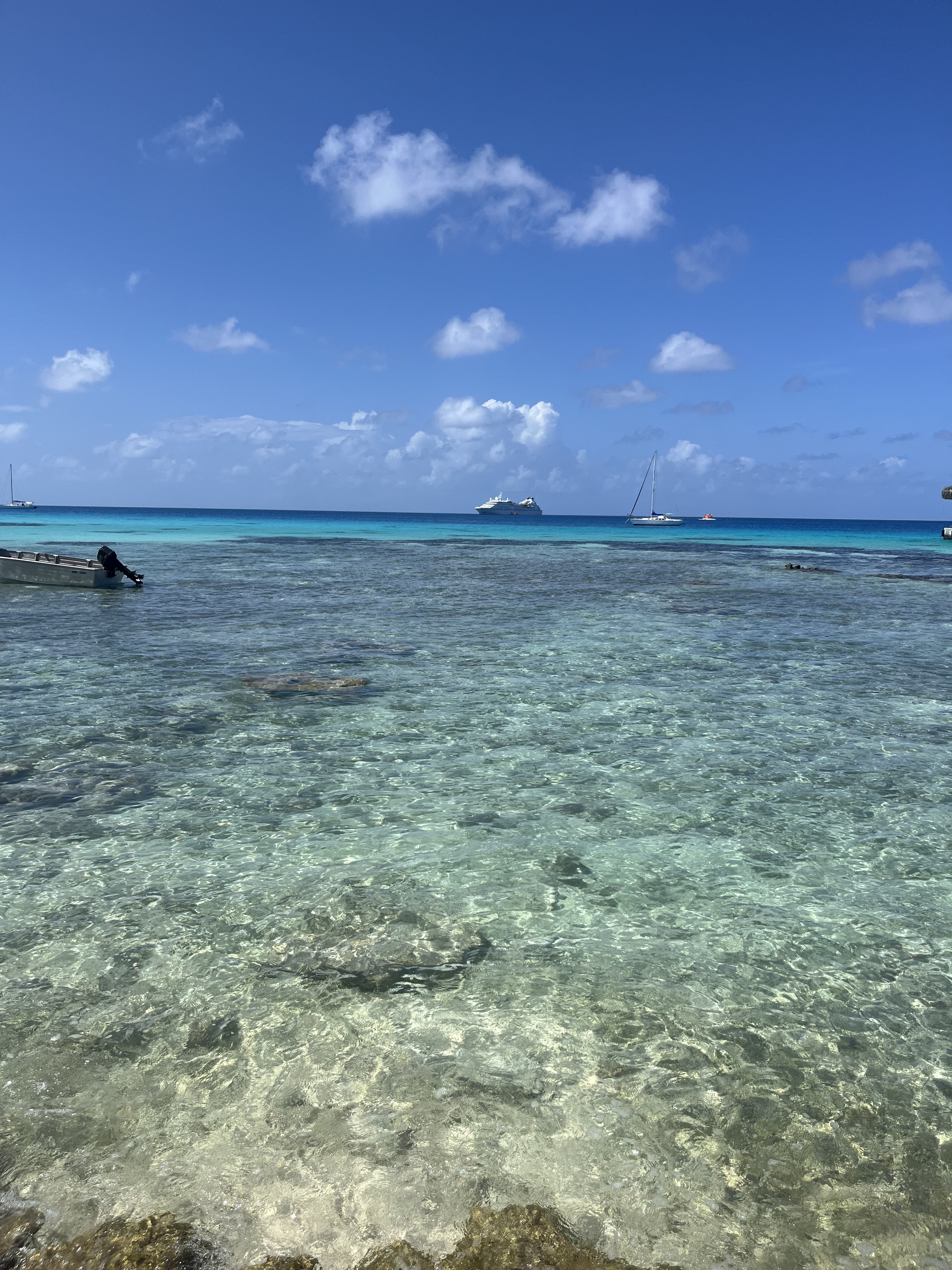 Crystal clear lagoon with coral heads and a boat under a bright Polynesian sky