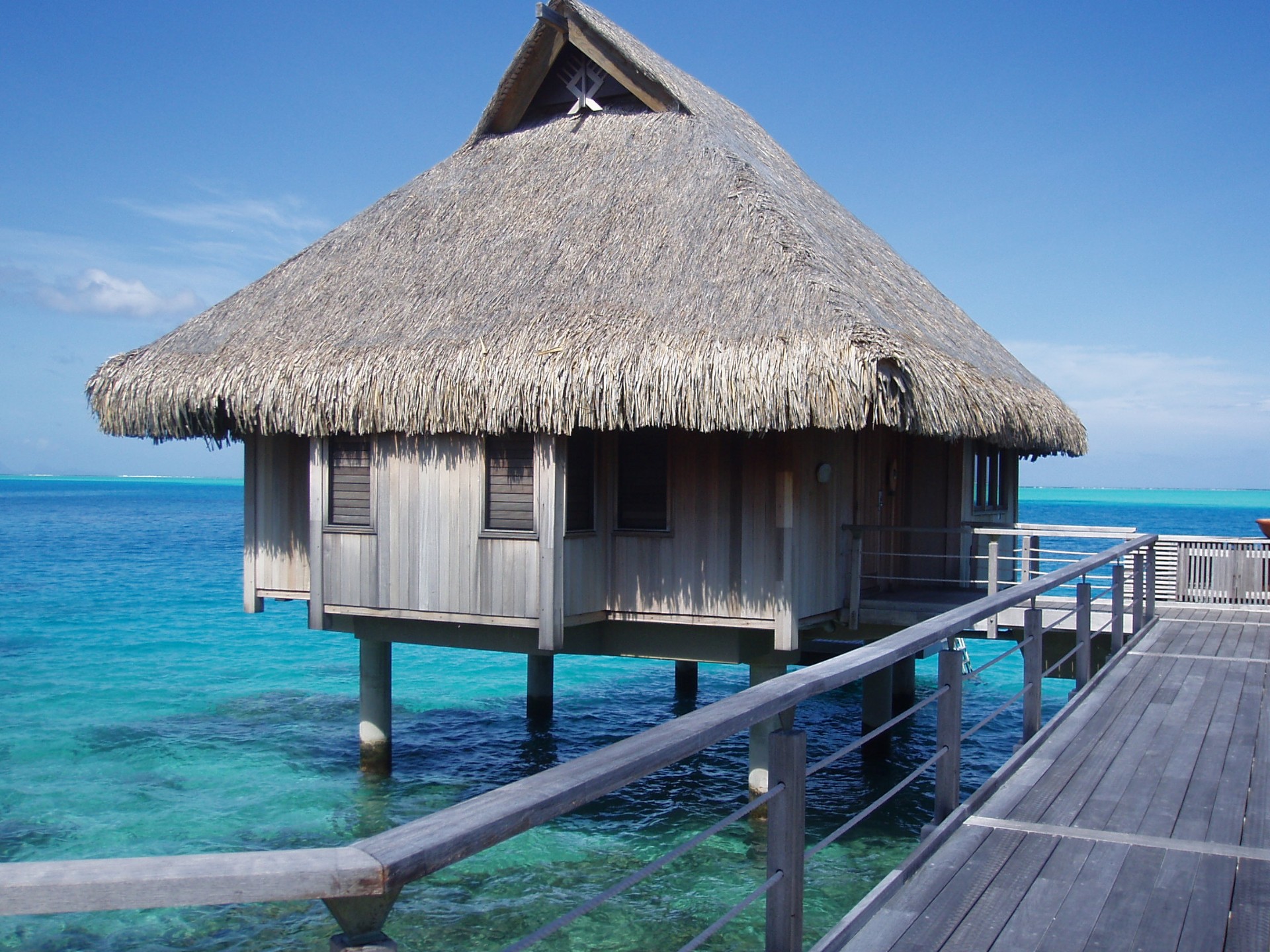Private overwater bungalow with thatched roof over calm lagoon